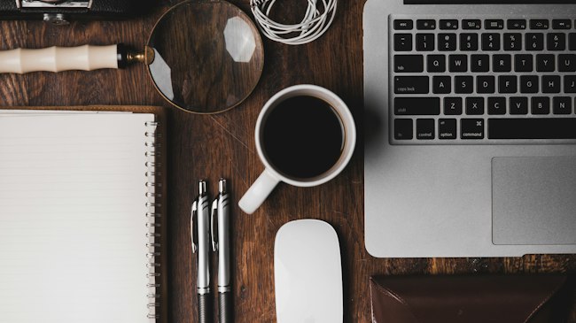 A desk with a laptop, notebook and coffee cup