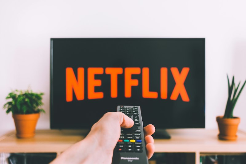A television showing the Netflix logo with a remote control pointed at it, representing a shared movie night