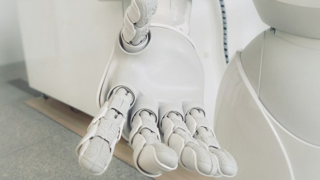A small humanoid robot figure standing on a desk next to a laptop
